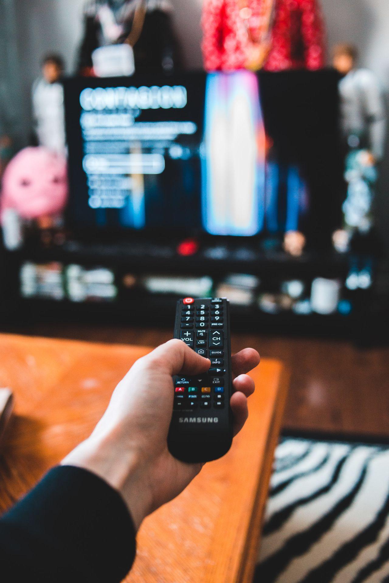 Mano sosteniendo un control remoto apuntando hacia una pantalla de televisión